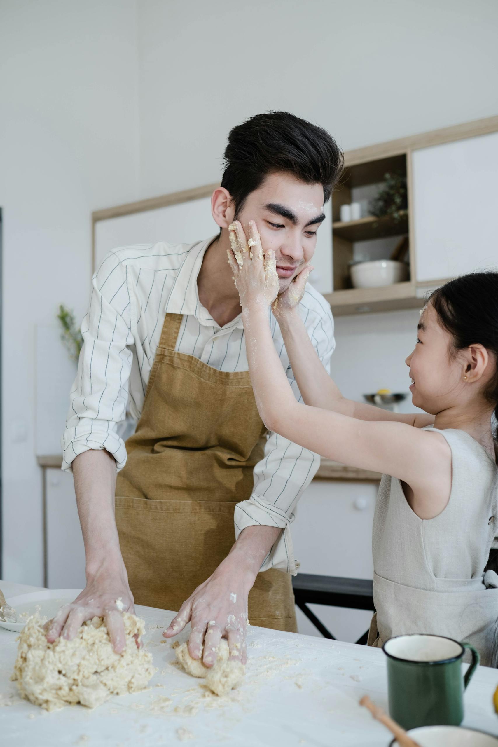 A father and daughter joyfully kneading dough together in their home kitchen, capturing a moment of playful family bonding.