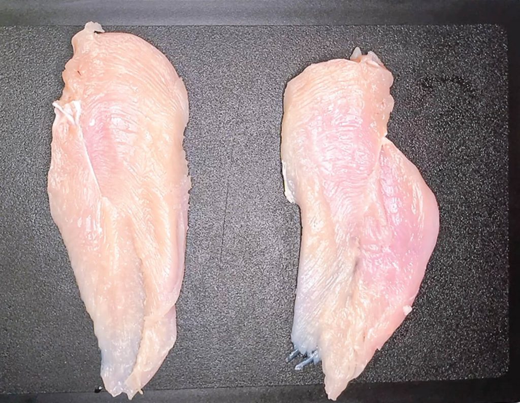 Butterflied chicken breasts laid flat on black cutting board."