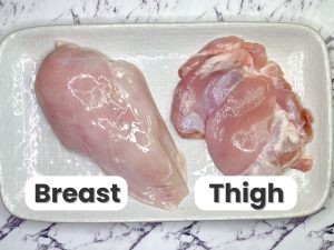 "Side-by-side comparison of raw chicken breast and chicken thigh on a tray, labeled to show the differences in cut and texture."
