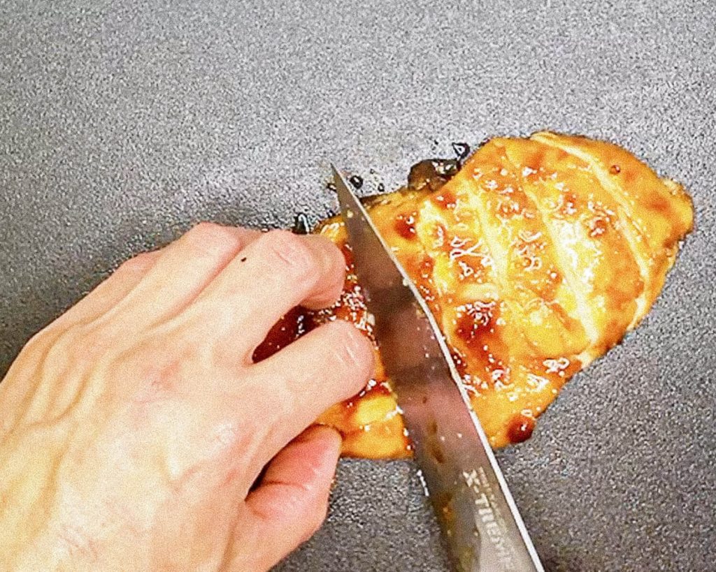 "Slicing juicy seared teriyaki chicken breast on a cutting board."
