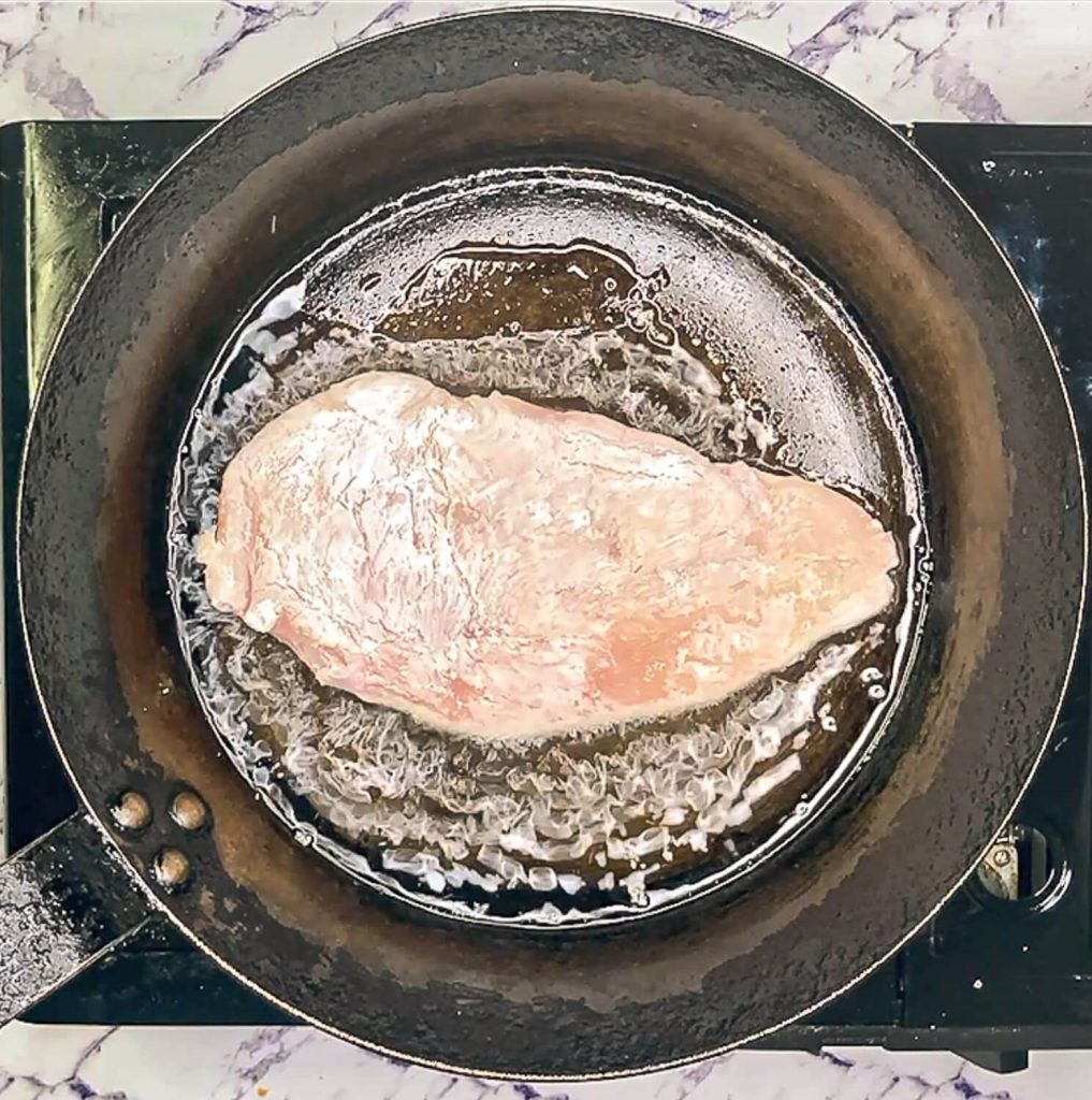 "Chicken breast searing in hot pan, just placed in oil."