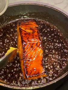 Adding fresh grated ginger to teriyaki sauce while basting salmon in a pan.