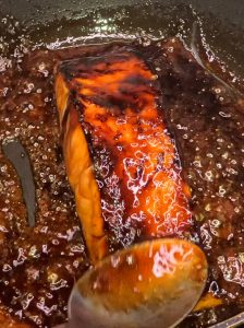Cooked salmon fillet coated in glossy ginger teriyaki sauce, ready to be plated.