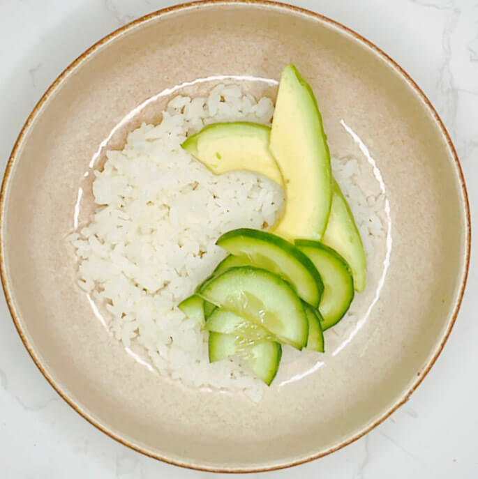 Cucumber and avocado slices arranged over steamed rice for a salmon bowl.