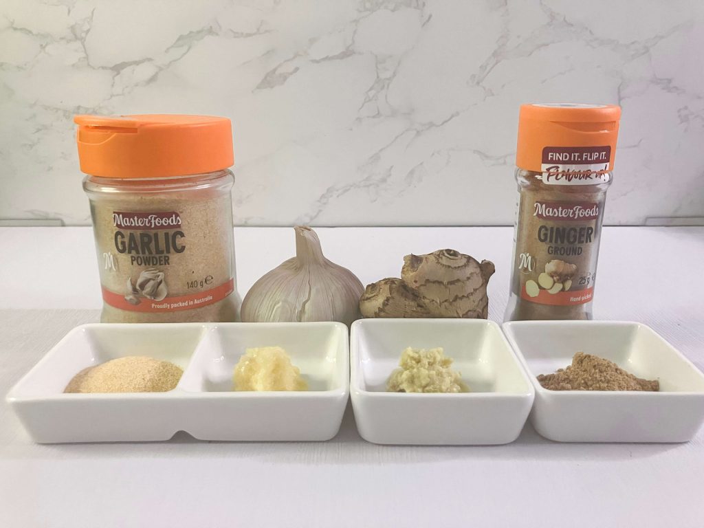 Fresh and powdered garlic and ginger displayed side-by-side – garlic powder, grated fresh garlic, grated fresh ginger, and ground ginger