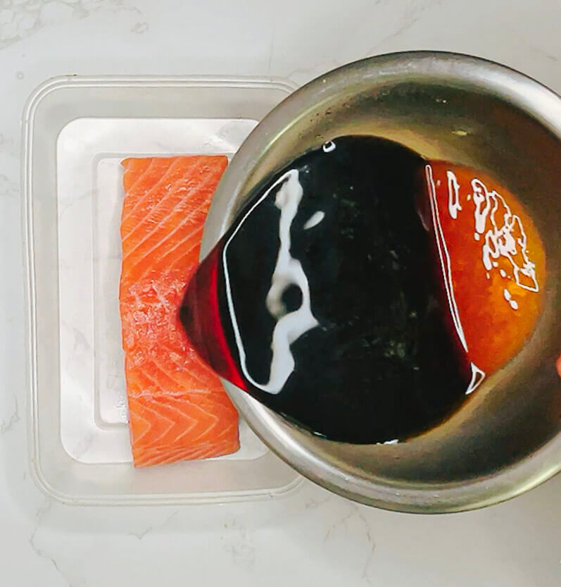 Pouring ginger teriyaki marinade over a raw salmon fillet in a container.