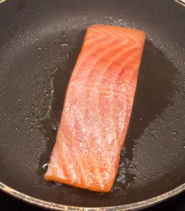 Raw salmon fillet placed on a hot pan at the beginning of the cooking process.