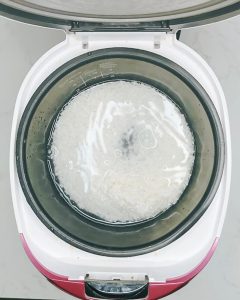 Short grain rice cooking inside a rice cooker for a salmon bowl.