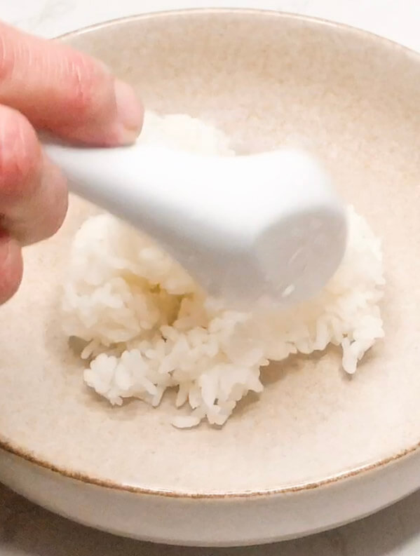 Scooping freshly cooked rice into a serving bowl as the base for a salmon bowl.