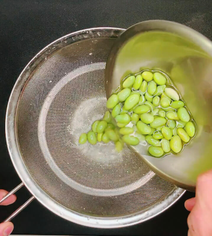 Edamame beans being strained in a mesh sieve during salad preparation.
