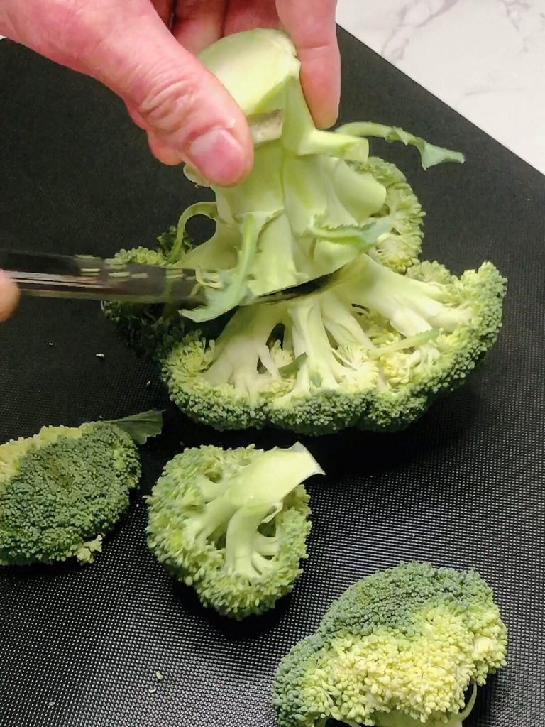 Hand holding broccoli stem while slicing into bite-sized florets for airfrying or roasting