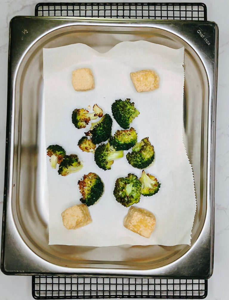 Tofu cubes added to tray with broccoli before oven roasting for teriyaki bowl