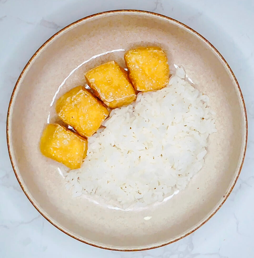 Crispy tofu cubes placed on top of steamed rice in bowl as first layer of teriyaki broccoli tofu