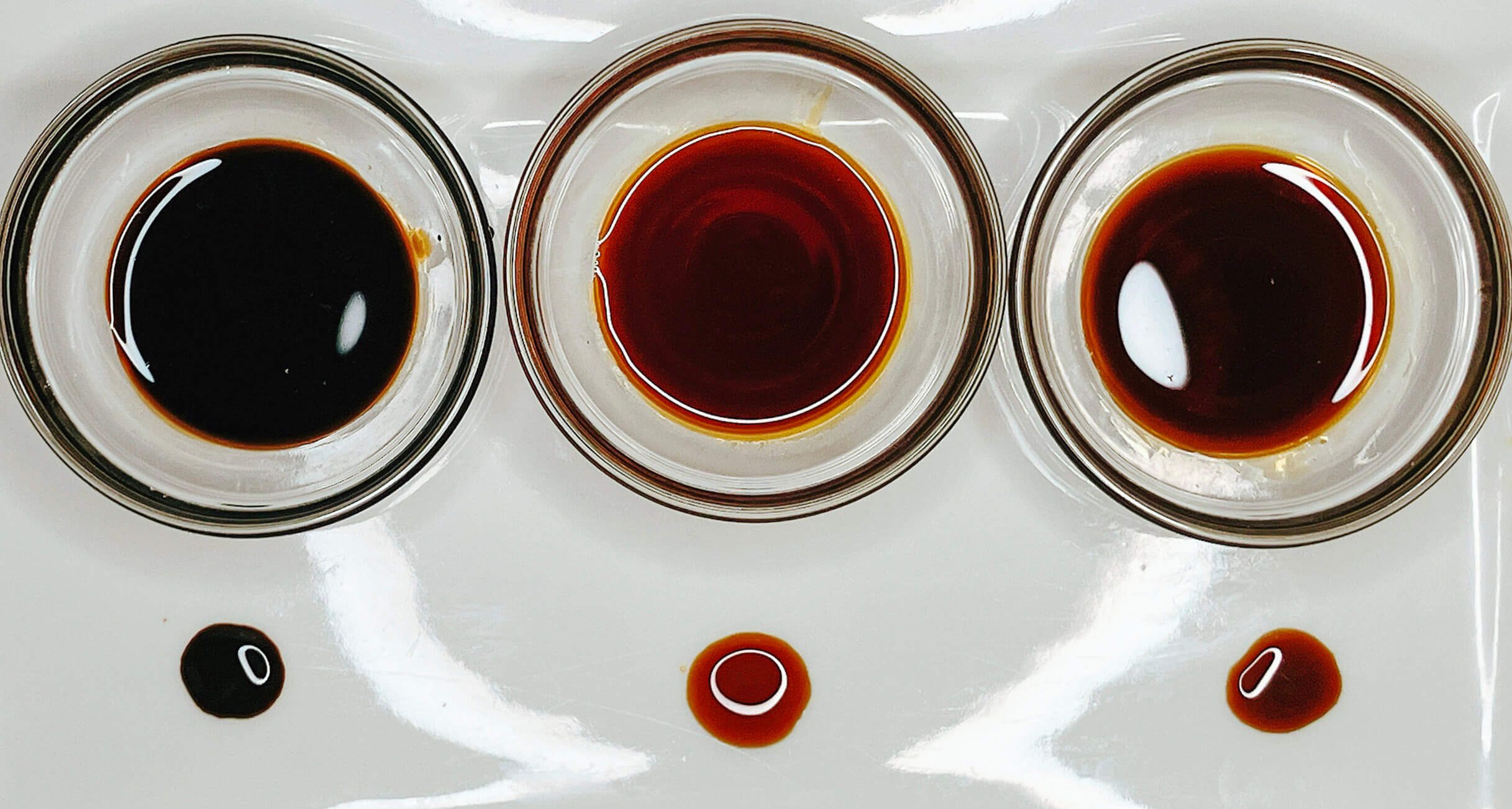 Soy sauce comparison showing tamari, gluten-free soy, and regular soy in glass bowls with drips underneath on white plate