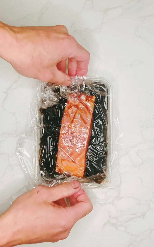 Wrapping marinated salmon in plastic to seal in the ginger teriyaki flavors.
