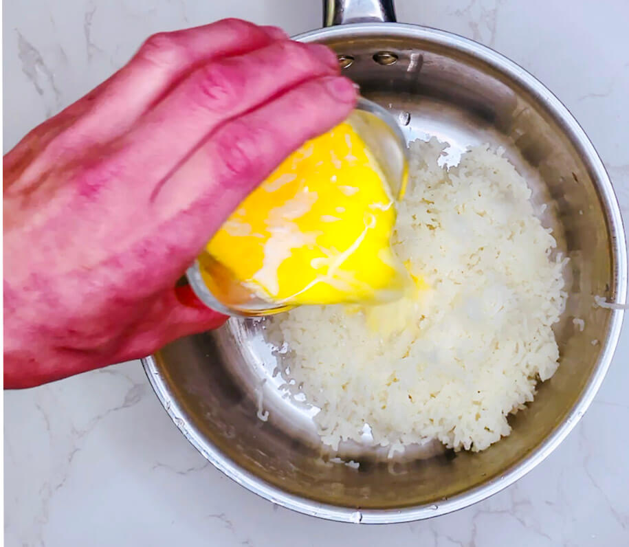 Hand adding a block of butter and pouring cream into a pot of riced potatoes to make mashed potatoes.
