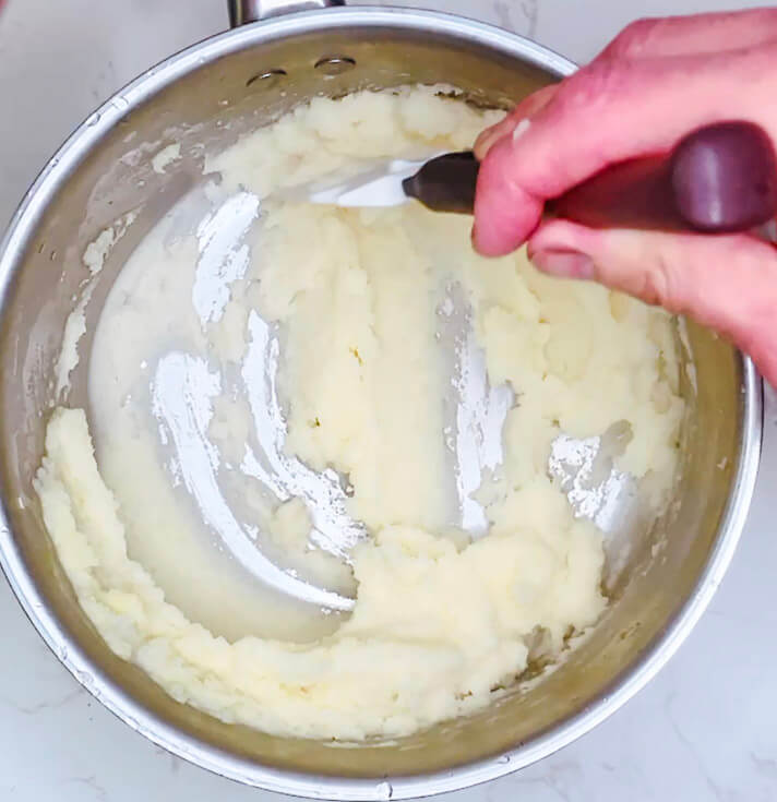 Hand mashing potatoes in a pot with a silicone spatula until smooth and creamy, final step in making mashed potatoes.