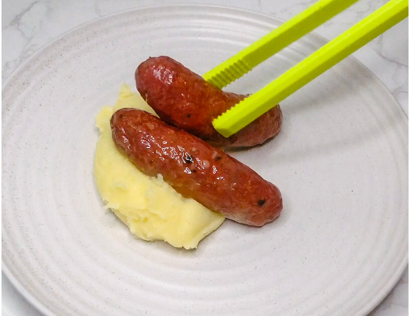 Using tongs to place cooked sausages on a mound of mashed potatoes for plating bangers and mash.