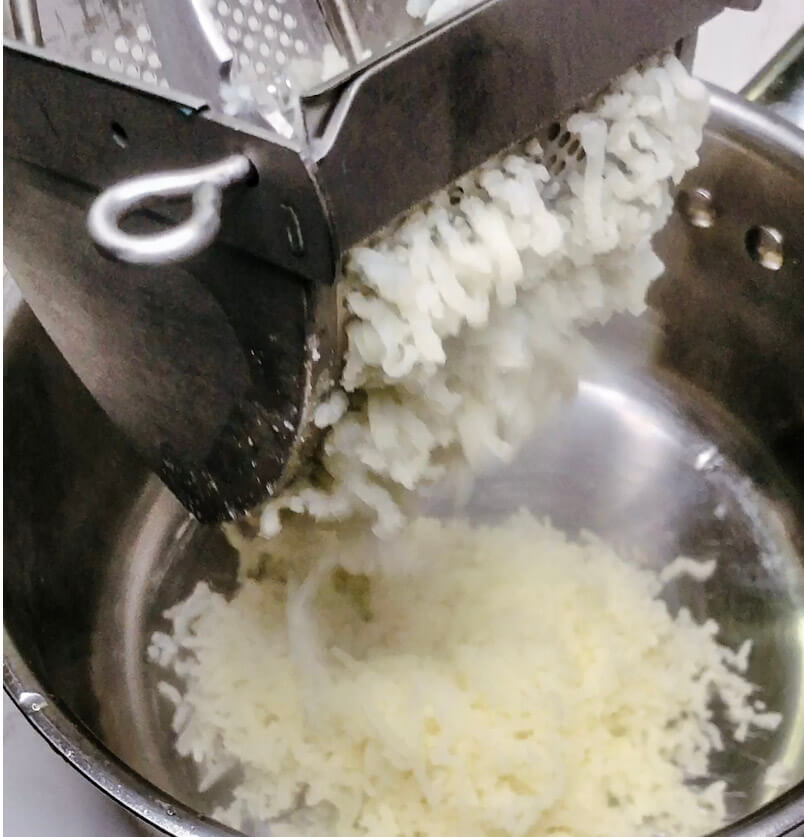 Riced potatoes falling into a pot during the mashing process, with melted butter visible underneath.