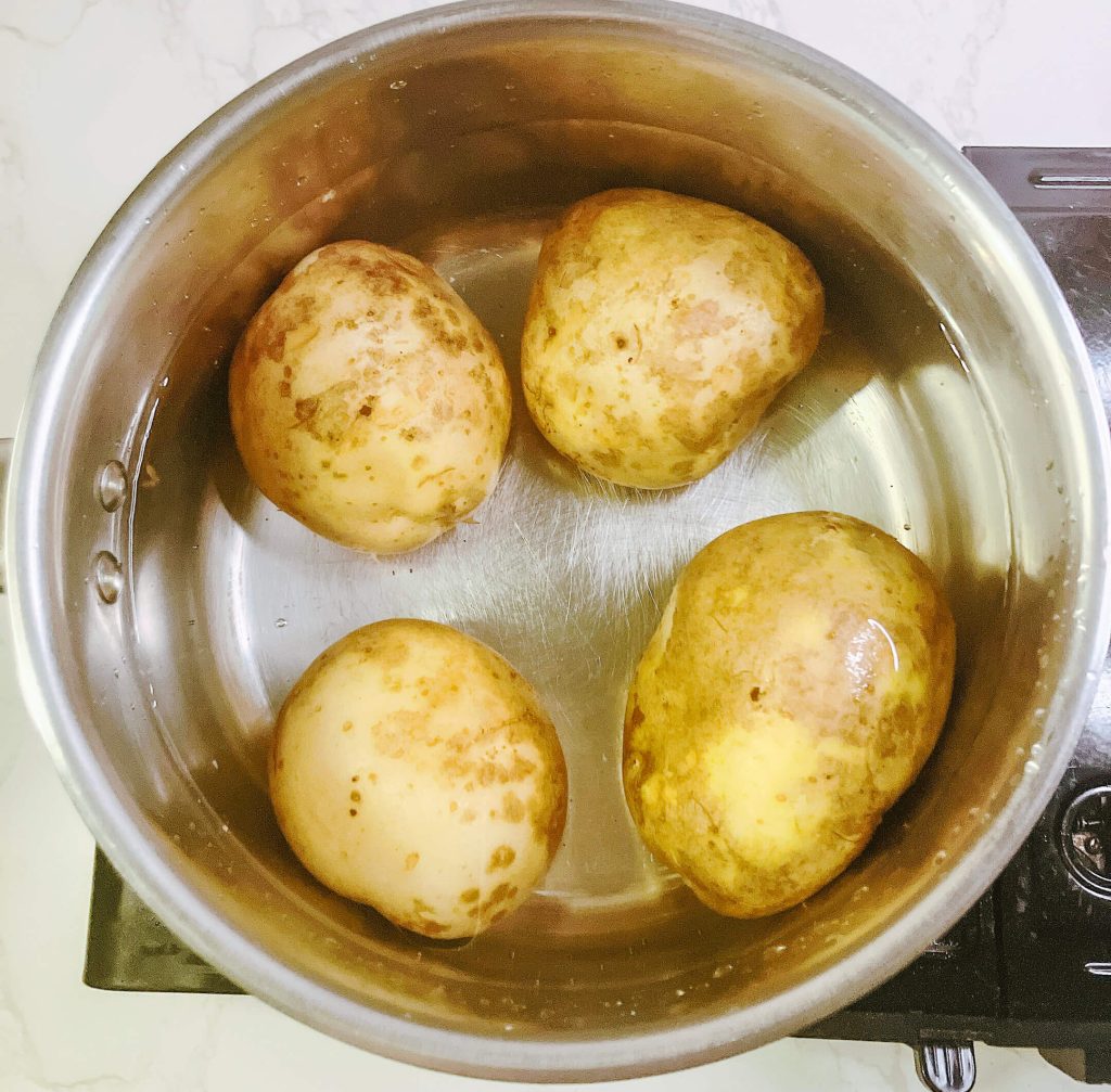 Boiling whole skin-on potatoes in a stainless steel pot for restaurant-style mashed potatoes.