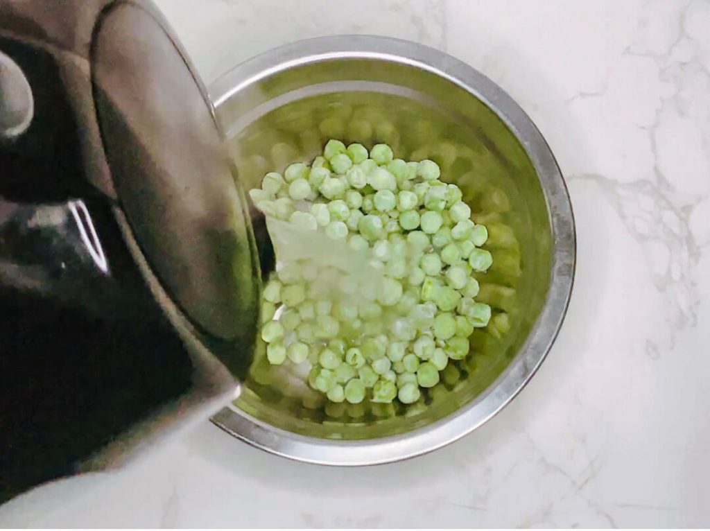 Frozen green peas being warmed in hot water inside a small saucepan as a quick side for bangers and mash.