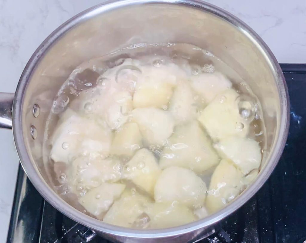 Chopped potatoes boiling in a stainless steel pot, preparing for mashed potatoes in bangers and mash recipe.