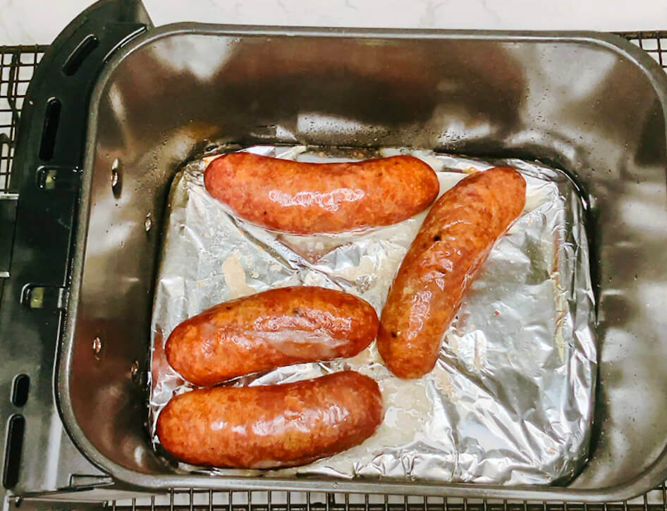 Cooked sausages resting on a foil-lined tray after air frying, golden and crisp for serving with mash and gravy.