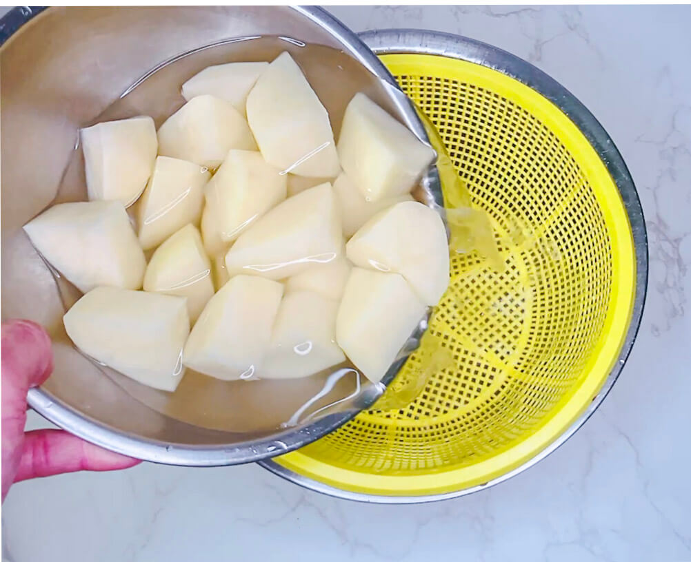 Rinsing peeled and chopped potatoes in a colander before boiling for mashed potatoes.