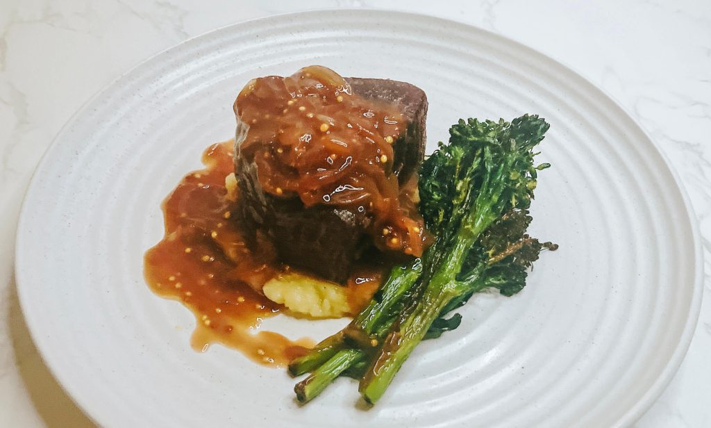 Seared steak served with mashed potatoes and broccolini, topped with teriyaki onion gravy — a hearty variation on the classic mash dish.