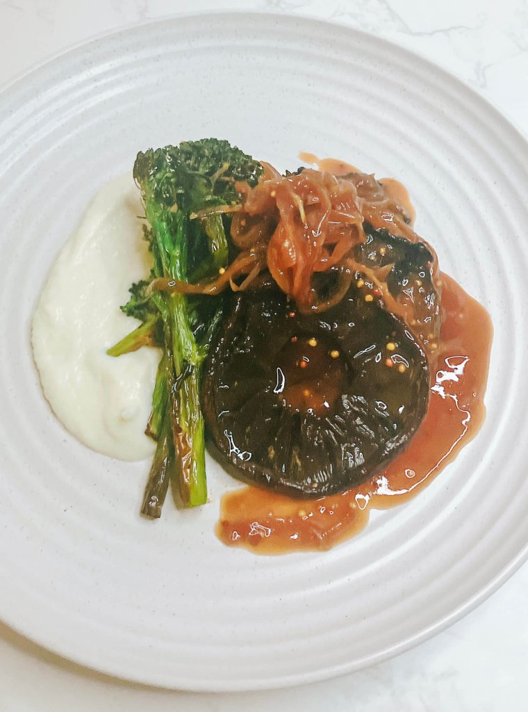 Mushroom steak served with cauliflower mash, air-fried broccolini, and teriyaki onion gravy on a white plate.