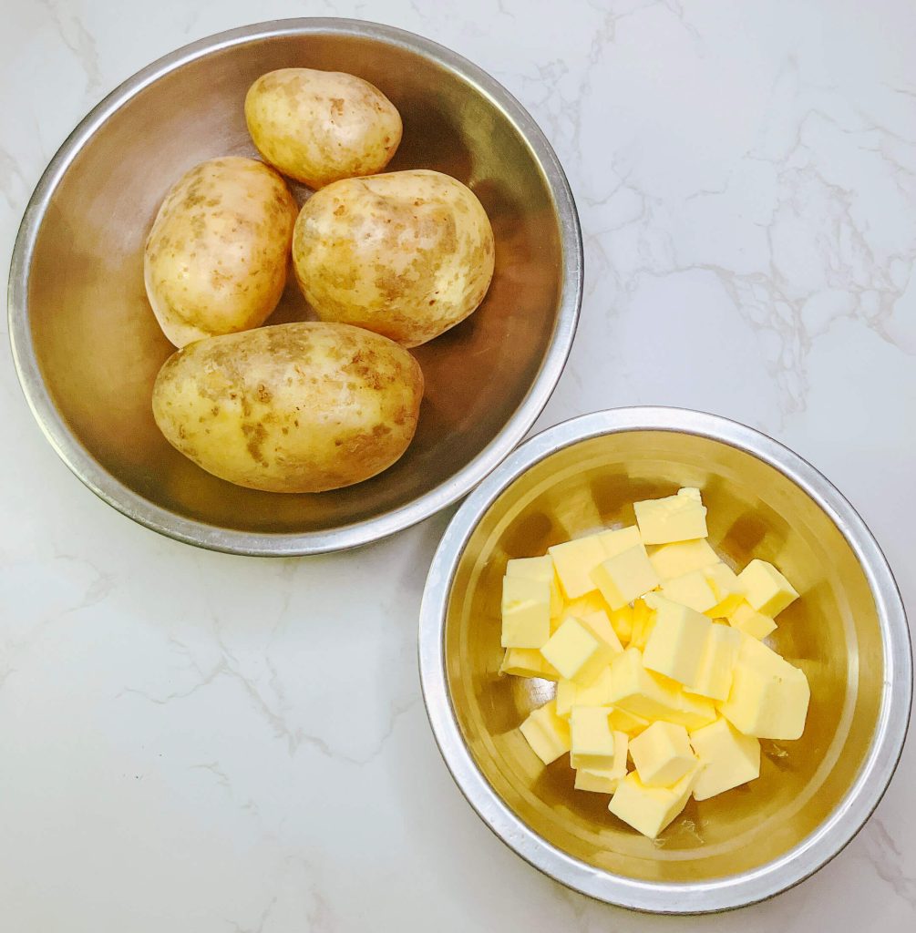 Boiled whole potatoes and cubed butter — simple ingredients for classic restaurant-style mashed potatoes.

