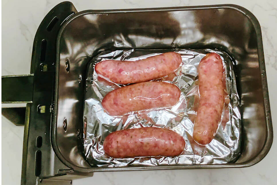 Raw pork sausages arranged in a foil-lined air fryer tray, ready to be cooked for bangers and mash.
