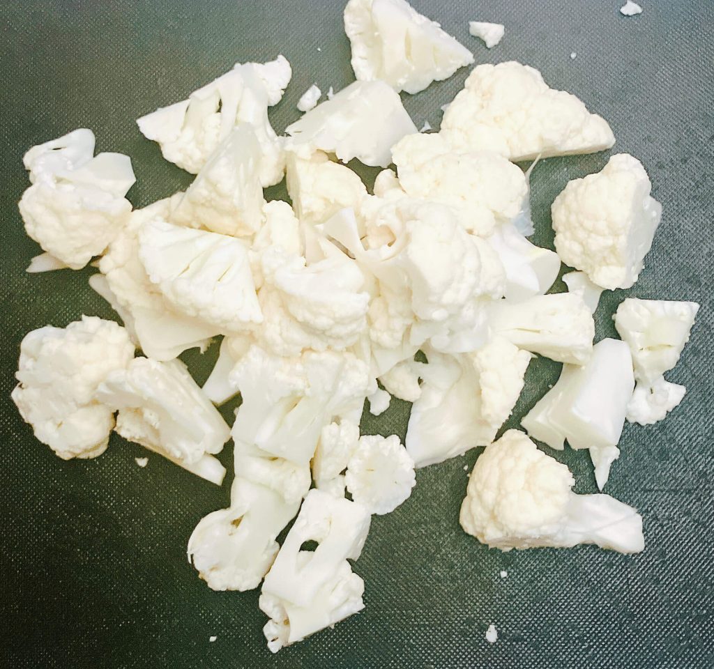 Chopped cauliflower florets on a cutting board, prepped for making creamy cauliflower mash.