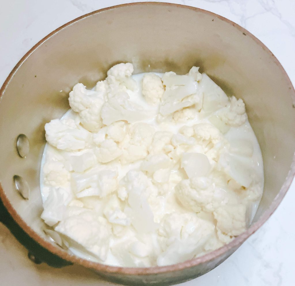 Cauliflower simmering in a pot with just enough cream to lightly cover the florets for mash.