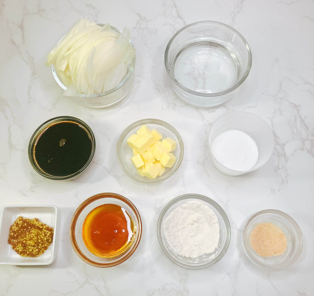 Flatlay of teriyaki onion gravy ingredients including soy sauce, water, golden syrup, sugar, flour, garlic powder, mustard, butter, and sliced onions.