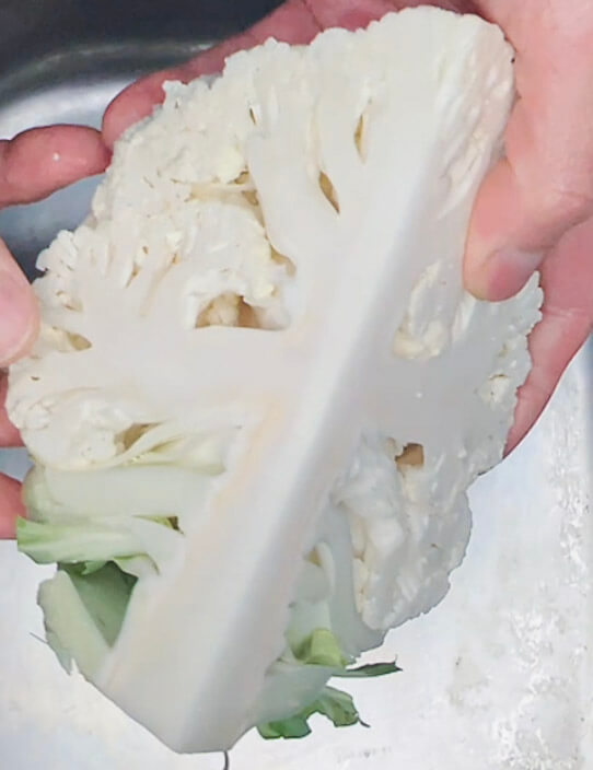 Cauliflower halved with core and stem attached, used as a handle for grating keto cauliflower rice.
