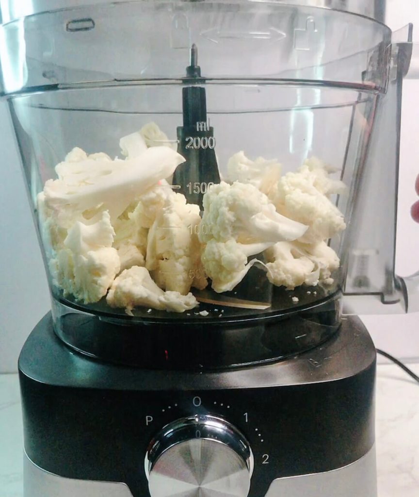 Cauliflower florets loaded into a food processor bowl, ready to be pulsed into keto cauliflower rice