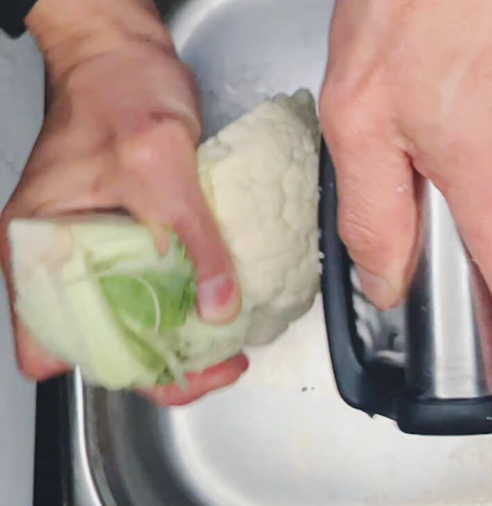 Hand holding a quartered cauliflower piece by the core to grate into keto cauliflower rice.”