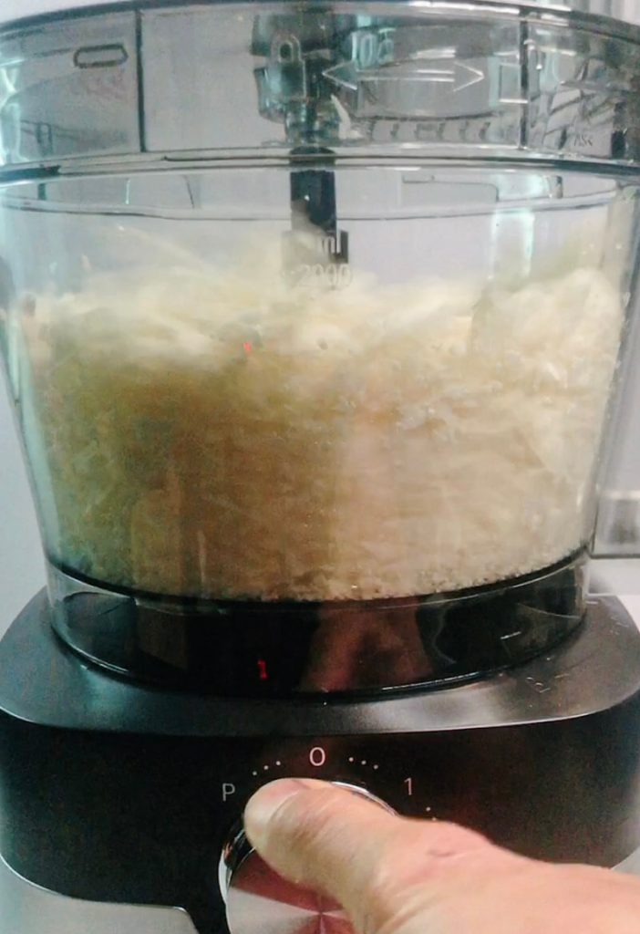 Cauliflower florets being pulsed in a food processor into rice-sized pieces for keto cauliflower rice.