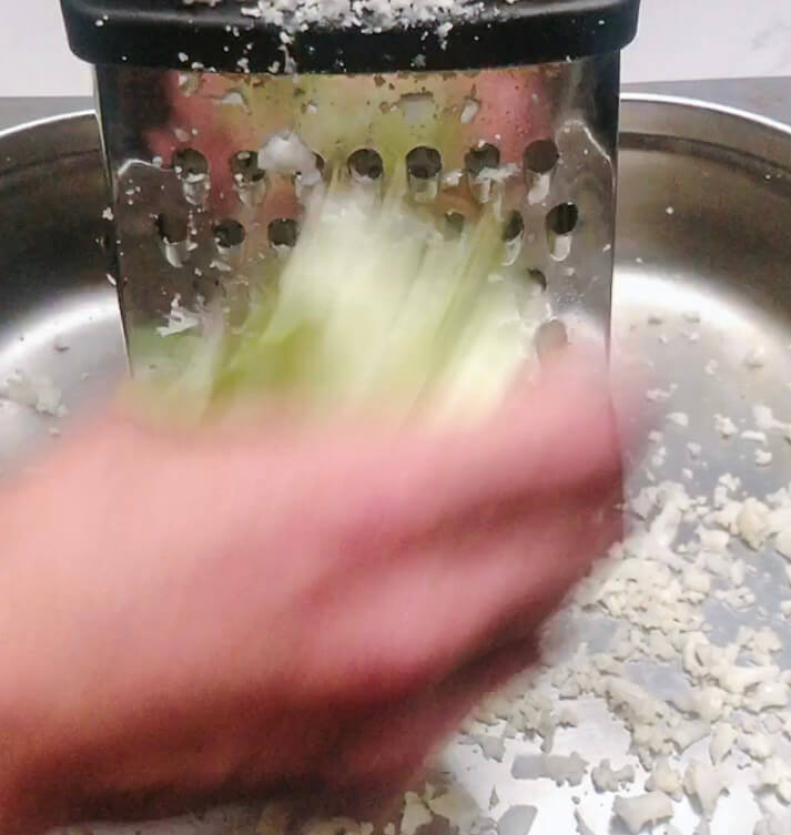 Quartered cauliflower being grated into rice-sized pieces over a bowl for keto cauliflower rice.”