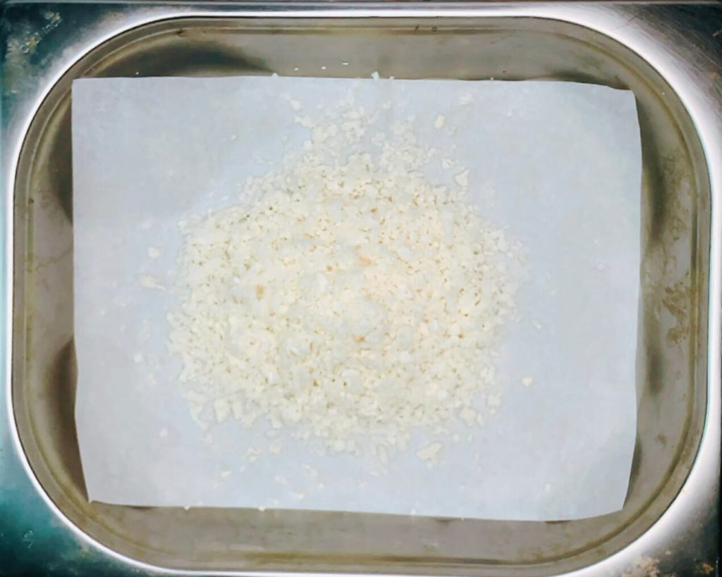 Raw cauliflower rice spread thinly on a tray before baking in the oven.”
