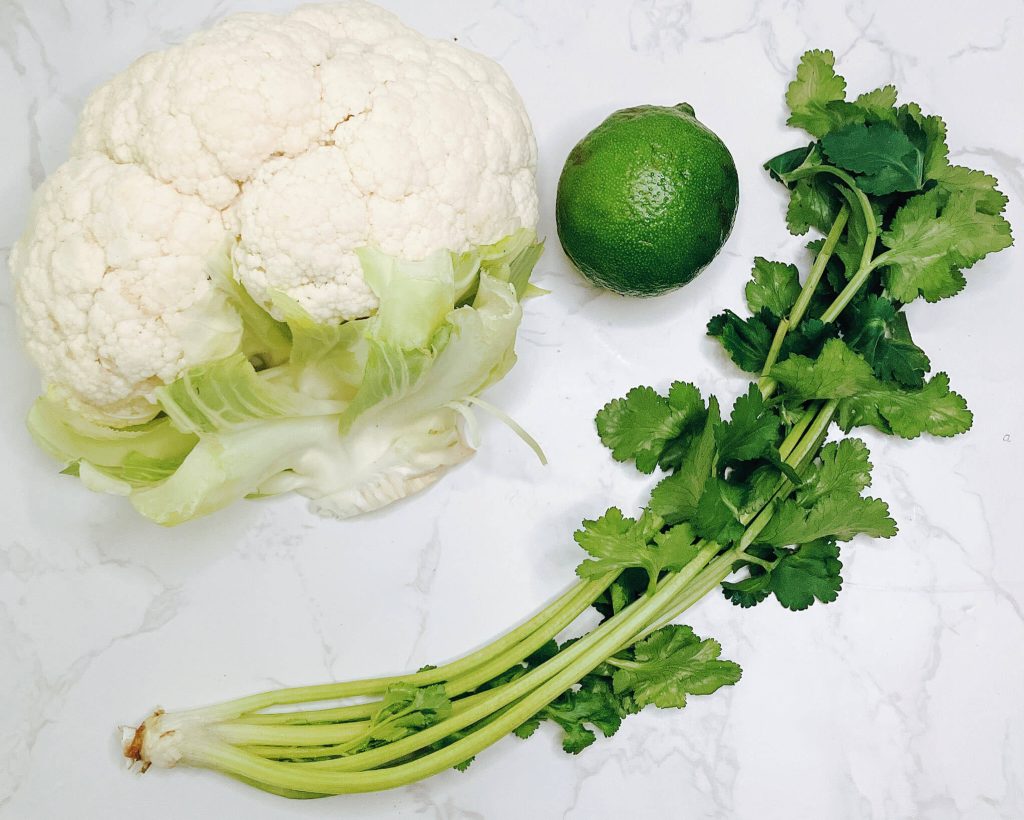 Whole cauliflower, lime, and cilantro ingredients for cauliflower rice in keto chicken katsu curry.