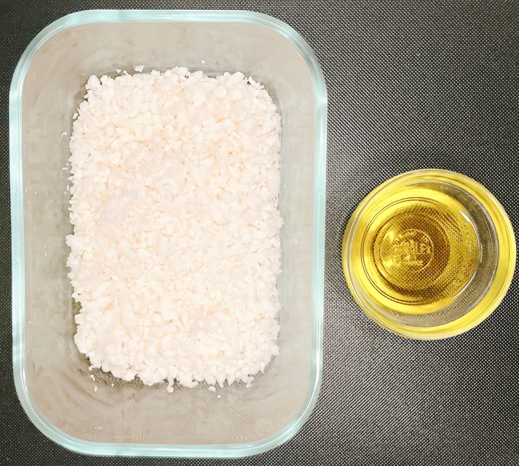 Ingredients for plain cauliflower rice – riced cauliflower in a glass container with a small bowl of oil.”