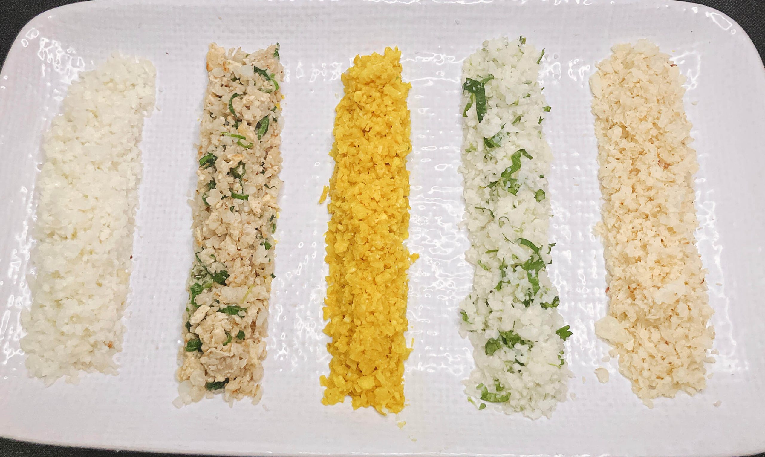 Five cauliflower rice variations on a white plate – plain, fried, turmeric, cilantro lime, and coconut.”