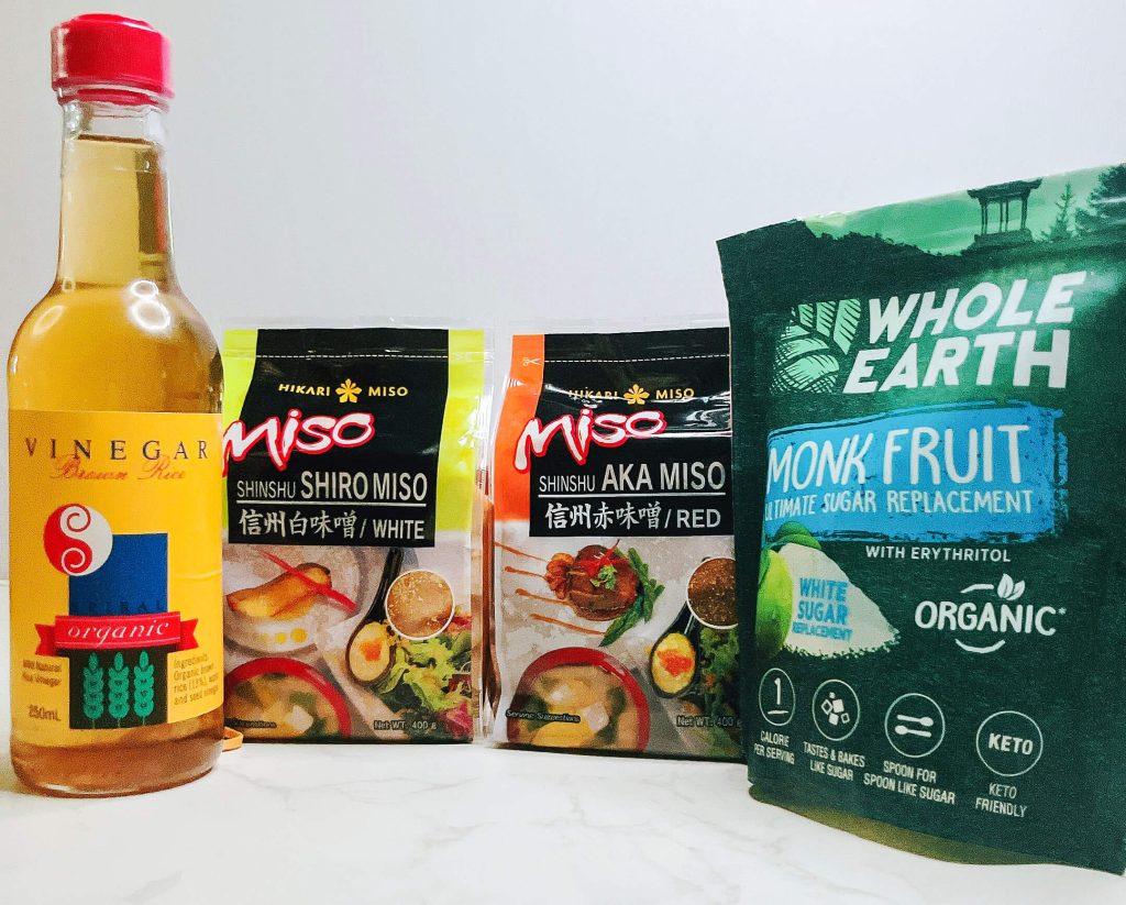 Top-down view of keto miso sauce ingredients including red miso paste, monk fruit sweetener, rice vinegar, and packaged keto-friendly pantry staples