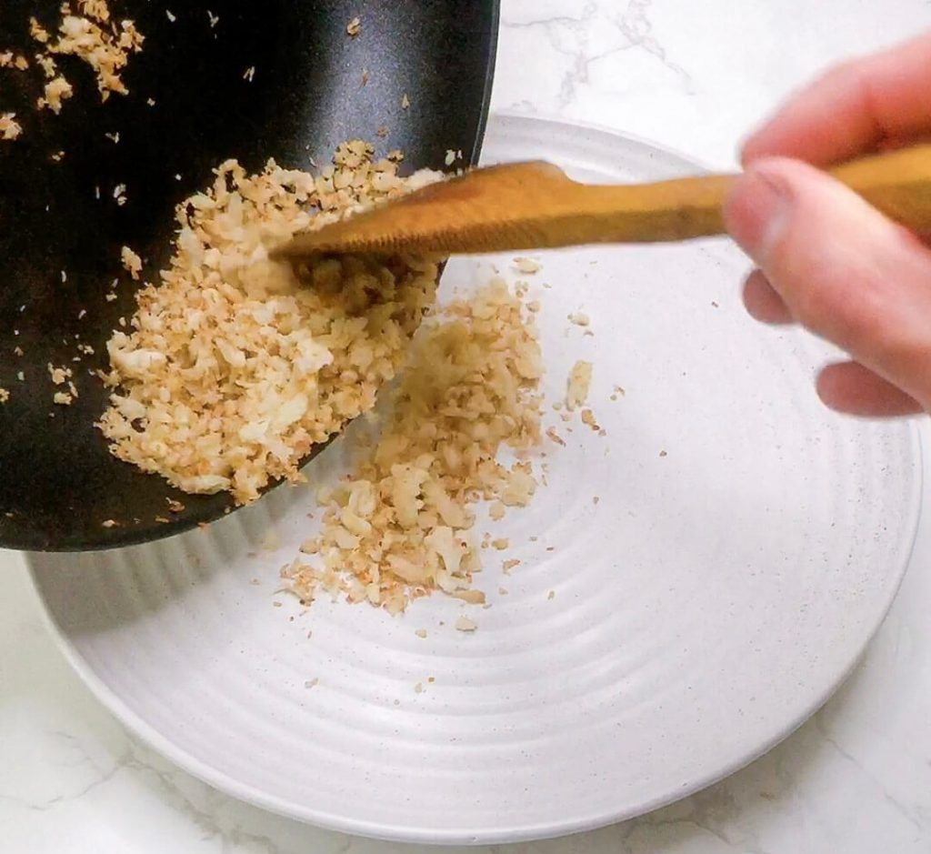 Spoon adding coconut cauliflower rice into a serving bowl.