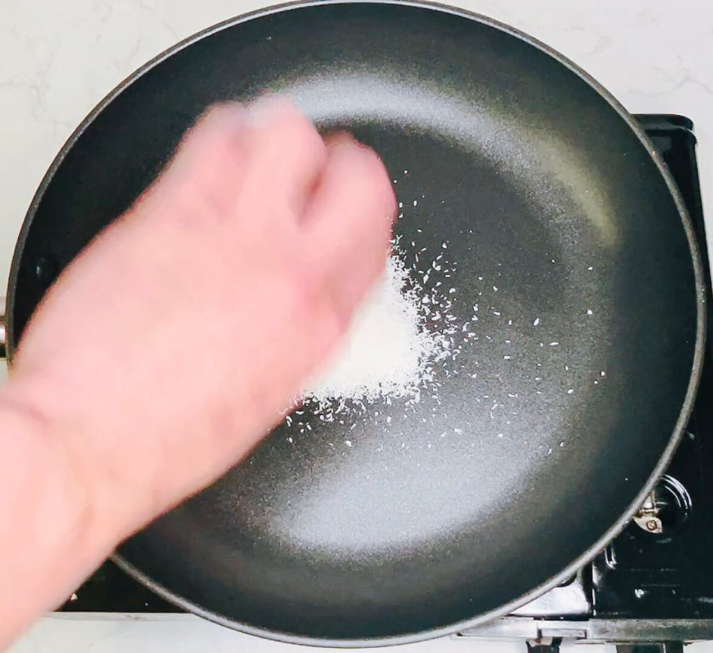 Hand sprinkling desiccated coconut into a dry non-stick pan.
