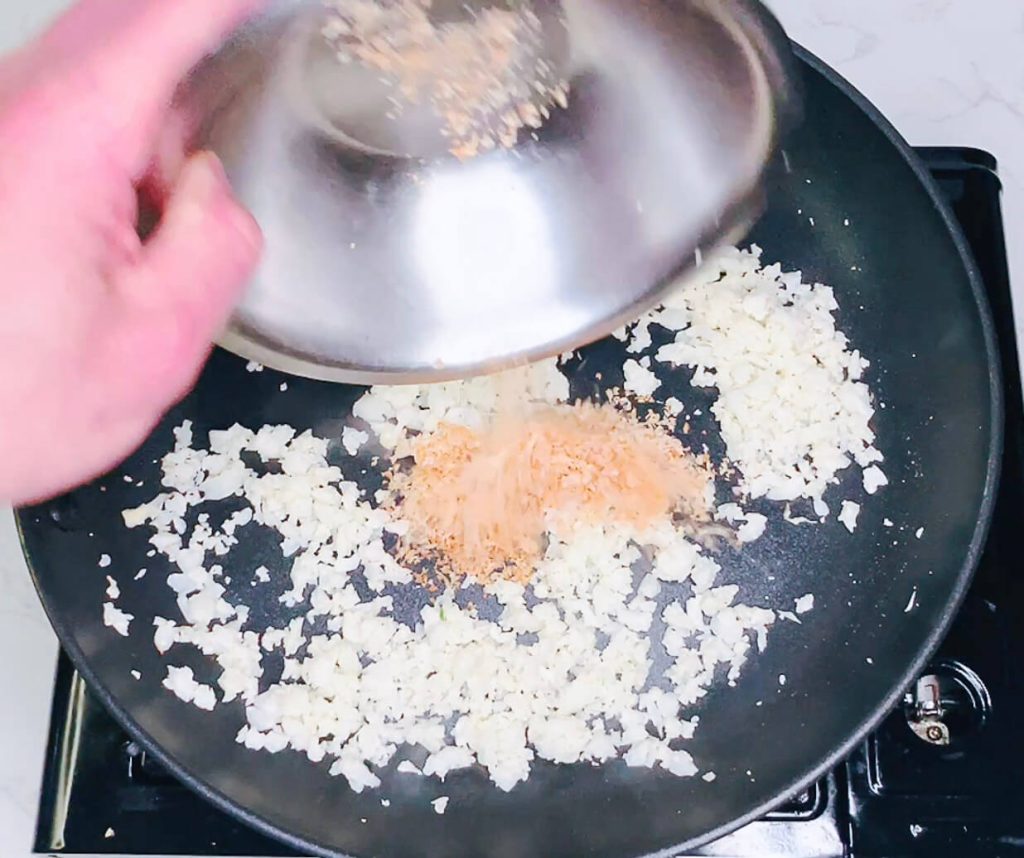 Toasted coconut being added back into the pan with cauliflower rice.