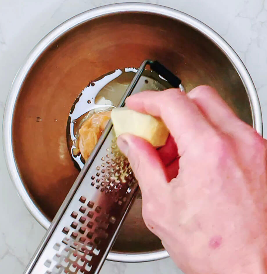 Grating fresh ginger into a bowl of miso marinade.