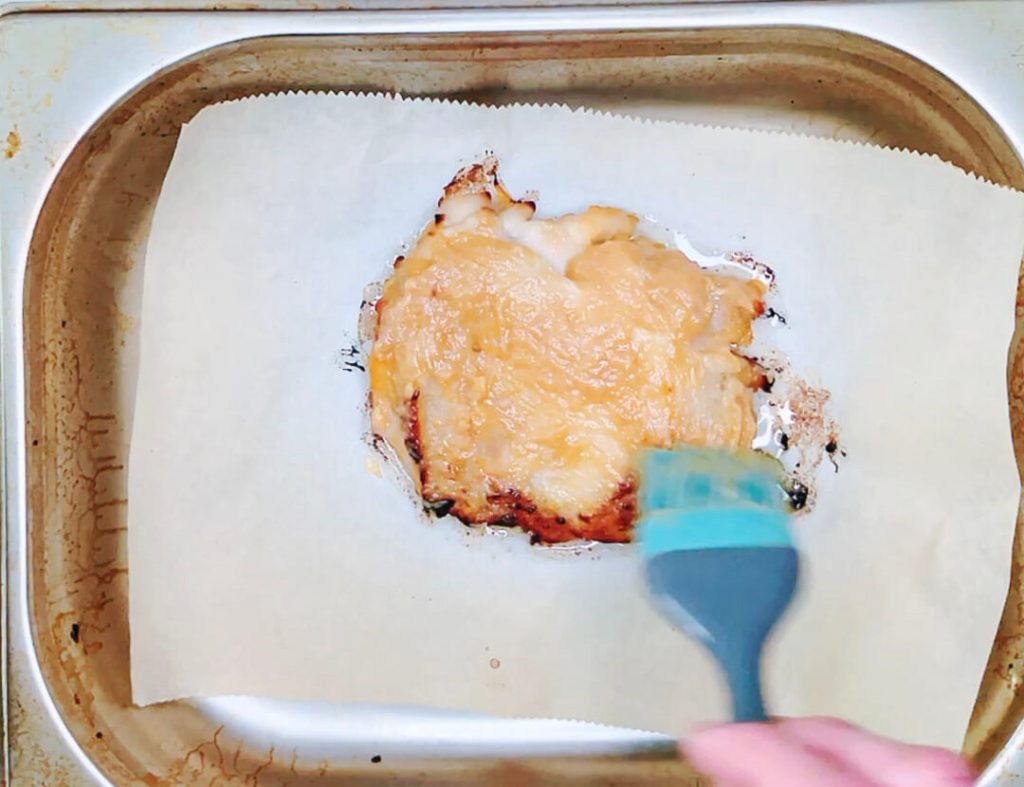 Brushing extra miso marinade onto chicken while it cooks in the oven.